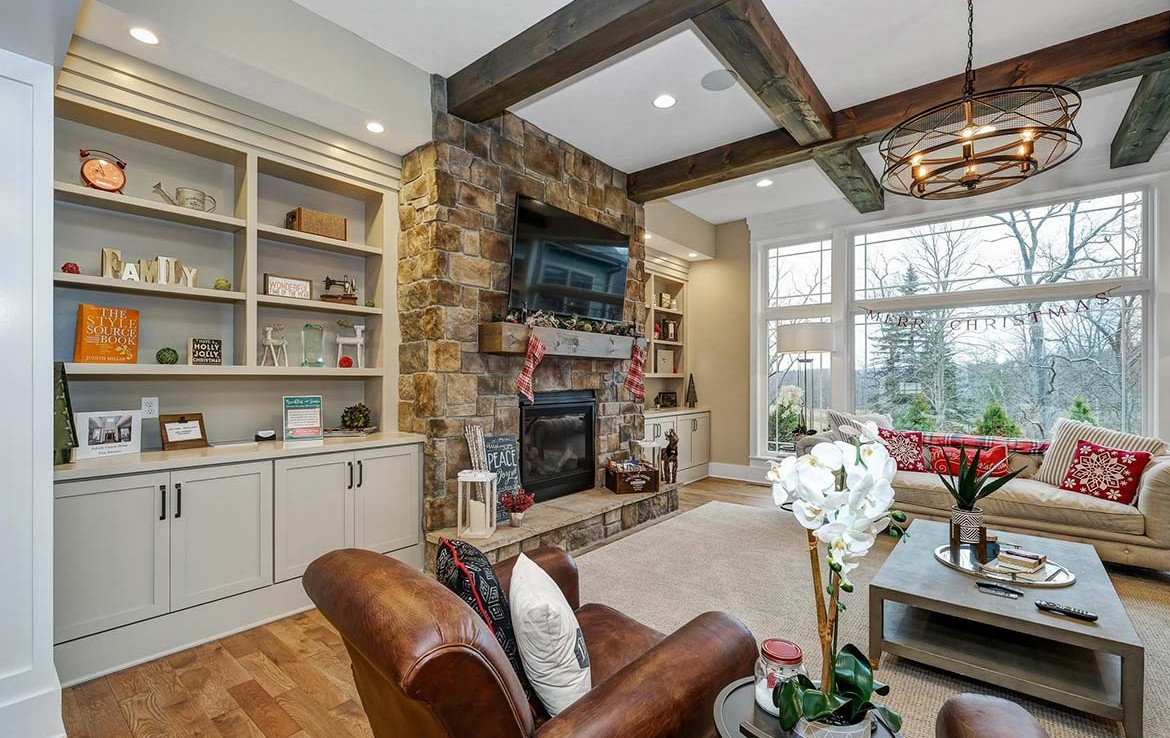 Austin Model Home at Forest Edge, Cranberry, PA, living room with gray builtins, stone fireplace, wooden beams in ceiling – Infinity Custom Homes