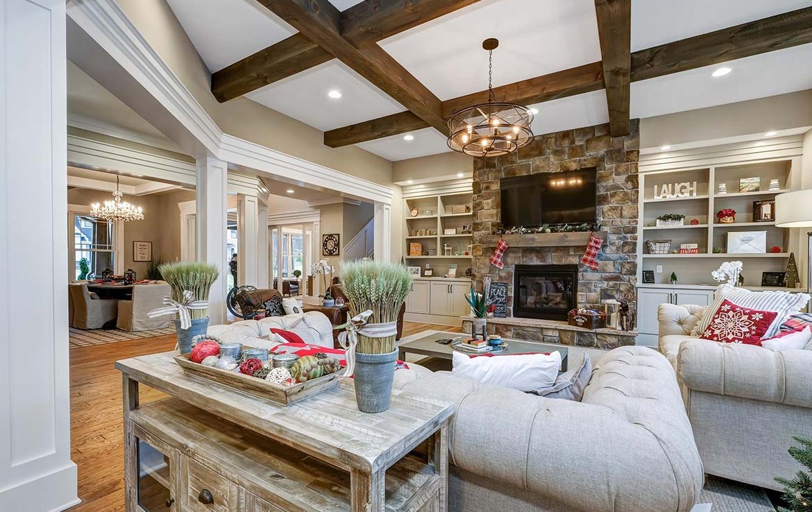 Austin Model Home at Forest Edge, Cranberry, PA, living room with white builtins, stone fireplace, wooden beams in ceiling – Infinity Custom Homes