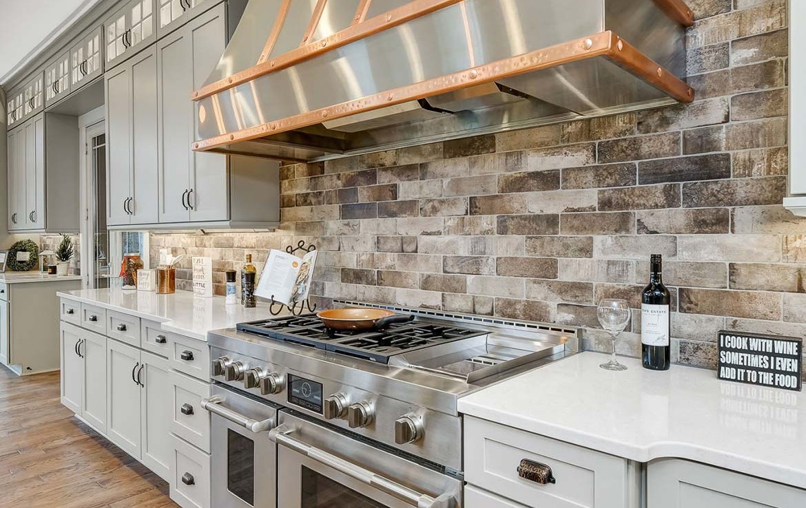Austin Model Home at Forest Edge, Cranberry, PA, luxury kitchen with gray cabinets, stone backsplash, and copper details – Infinity Custom Homes